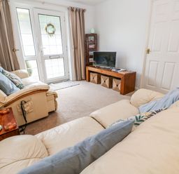 A living room with two cream sofas a wooden TV stand with baskets and a lamp on a side table at Brook Haven Rosecraddoc Lodge near Liskeard Cornwall