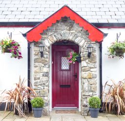 The front entrance of a cottage with a red door stone arch and hanging flower baskets at Cookies Cottage in Ballyshannon County Donegal