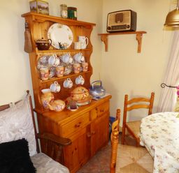 A dining area with wooden chairs a wooden cabinet with cups plates and teapots a table with floral tablecloth and flowers at Cookies Cottage Ballyshannon County Donegal