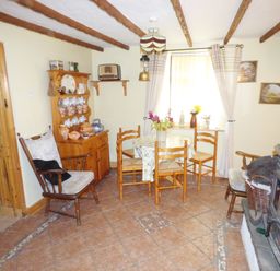 A dining area with a round table and chairs a wooden cabinet with crockery a window with curtains and a wood burning stove at Cookies Cottage in Ballyshannon County Donegal