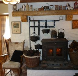 A room with a wood burning stove a rocking chair baskets of firewood and hanging pots at Cookies Cottage Ballyshannon County Donegal