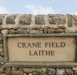 A stone wall with a sign reading Crane Field Laithe Otterburn North Yorkshire