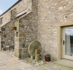 A stone patio with outdoor chairs pots of flowers and an old millstone at Crane Field Laithe in Otterburn North Yorkshire