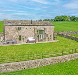 A stone-built house with a patio garden lawn outdoor seating and hot tub surrounded by stone walls in a rural field at Crane Field Laithe in Otterburn North Yorkshire