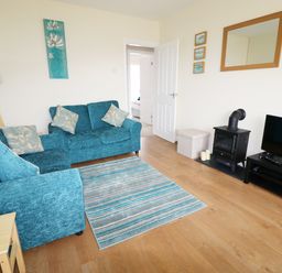 A living room with two blue sofas a floor lamp a small wood stove candles and a television at Anneddle in Four Mile Bridge