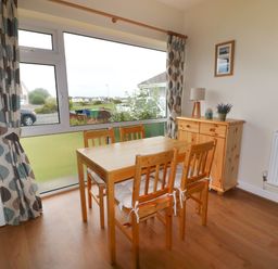 A dining area with a wooden table and four chairs next to a large window with patterned curtains at Anneddle in Four Mile Bridge