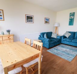 A dining area with wooden table and chairs next to a living space with blue sofas and a rug at Anneddle in Four Mile Bridge