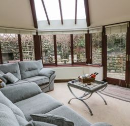 A room with two grey sofas a glass coffee table and large windows overlooking a stone wall at Hill Bank in Hutton Roof