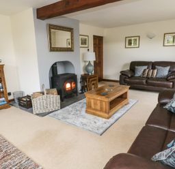 A living room with leather sofas a wood burning stove and a bookshelf at Hill Bank in Hutton Roof