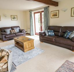 A living room with two leather sofas a wooden coffee table and firewood at Hill Bank in Hutton Roof