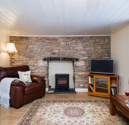 A living room with a leather armchair stone fireplace TV on wooden stand and a wooden coffee table with wine glasses at 3 Horse Pool Road in Laugharne