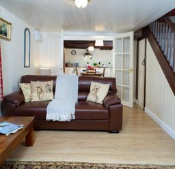 A living room with a brown leather sofa and cat-themed cushions at 3 Horse Pool Road in Laugharne