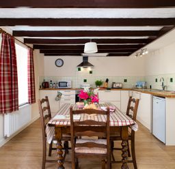 A kitchen with wooden table and chairs a checked tablecloth and red plaid curtains at 3 Horse Pool Road in Laugharne