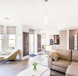 A living room with a sectional sofa coffee table with flowers a chair and kitchen in the background at No 6 Arlington Villas in Ilfracombe