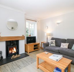 A living room with a fireplace a gray sofa wooden tables and a television at Glan Dwr in Red Wharf Bay