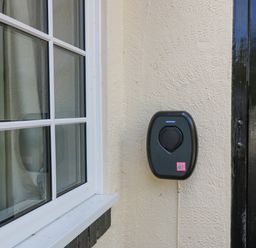 An electric vehicle charging station mounted on an exterior wall between a window and a black door at Glan Dwr in Red Wharf Bay