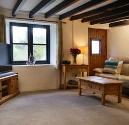 A living room with a sofa a wooden coffee table a television on a wooden stand and a side table with flowers at Easterly Cottage in Bude