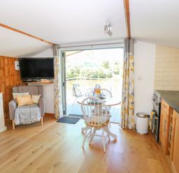 A small kitchen and dining area with a table and chairs and an armchair next to a wall-mounted television at Lakeside Lodge East Harling near Thetford
