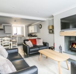 A living room with black leather sofas a wooden coffee table a fireplace with a fire and a wall-mounted TV at Ivy Bank in Windermere