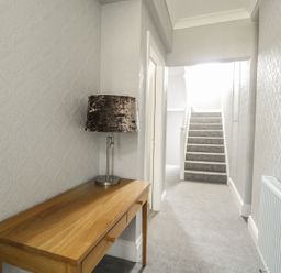 A hallway with a wooden table and lamp next to carpeted stairs at Ivy Bank in Windermere