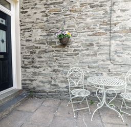 An outdoor area with a black door numbered 86 a hanging basket with flowers and a white metal table with two matching chairs at Ivy Bank in Windermere