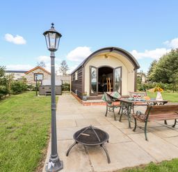 An outdoor patio with a table and benches with a small building and lamp posts in a garden at Meadow View in Rhayader