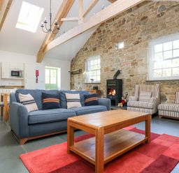 A living room with a blue sofa wooden coffee table fireplace and exposed stone walls at Wheal Grey in Praa Sands
