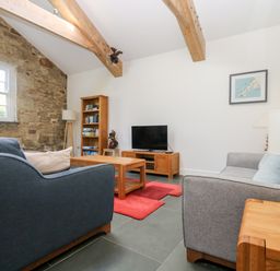 A living room with wooden beams stone wall sofas and a television at Wheal Grey in Praa Sands