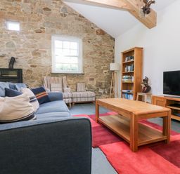 A living room with a blue sofa striped armchairs wooden coffee table bookshelf and television at Wheal Grey in Praa Sands