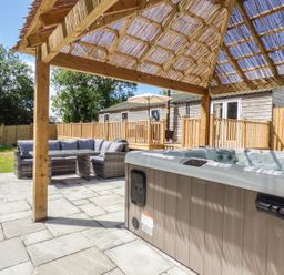 A patio with a hot tub and outdoor seating under a wooden pergola at Kelyow in St Day