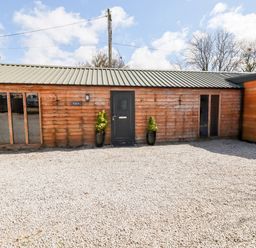 A wooden building with a dark door and windows on a gravel area at Kelyow in St Day