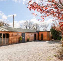 A single-story wooden building with a gravel driveway and plants at Kelyow in St Day