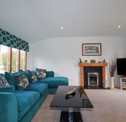 A living room with a teal sofa with floral cushions a black coffee table a fireplace and a TV at Kelyow in St Day