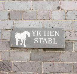 A wall sign with a horse illustration and the text YR HEN STABL on a brick wall at Hen Stabl in Llanrwst