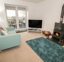 A living room with a teal sofa a blue rug a wood burning stove a television and patio doors opening to a balcony at Hen Stabl in Llanrwst