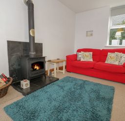 A living room with a red sofa a wood burning stove and a blue rug at Hen Stabl in Llanrwst