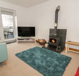 A living room with a wood stove a teal rug a television and seating at Hen Stabl in Llanrwst