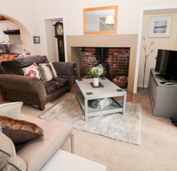A living room with two sofas a coffee table a fireplace a television and a grandfather clock at Corbett Cottage in New Haggerston near Holy Island