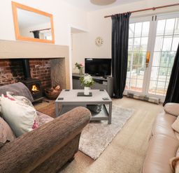A living room with sofas a coffee table a fireplace and a television at Corbett Cottage in New Haggerston near Holy Island