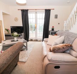 A living room with sofas a coffee table flowers a television and stairs at Corbett Cottage in New Haggerston near Holy Island