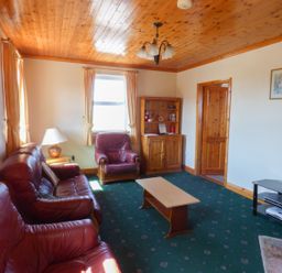 A living room with red leather sofas a wooden coffee table a wooden cabinet and a TV stand at Seaview Cottage in Fanore County Clare