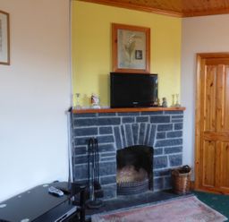 A room with a stone fireplace a television on the mantel a wooden door and a black table with remotes at Seaview Cottage Fanore County Clare