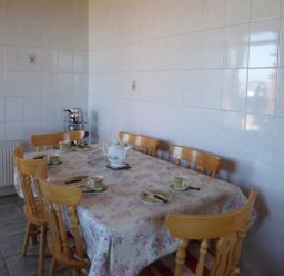 A dining room with a table covered in floral tablecloth six wooden chairs cups plates and a teapot at Seaview Cottage in Fanore County Clare
