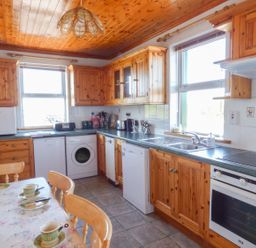 A kitchen with wooden cabinets appliances and a dining table with cups at Seaview Cottage in Fanore County Clare