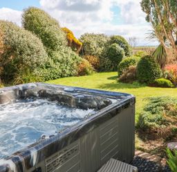 A bubbling hot tub next to a garden with grass and various bushes at The Beach House Criccieth