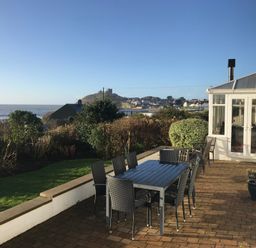 An outdoor patio with a dining table and chairs overlooking a garden and distant castle at The Beach House Criccieth