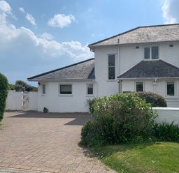A white two story house with a paved driveway and shrubs in the front garden at The Beach House Criccieth