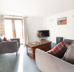 A living room with grey sofas and a wooden coffee table with flowers and a TV at Lower West Curry Cottage in Launceston