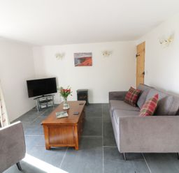 A living room with a gray sofa, wooden coffee table, television, and curtains at Lower West Curry Cottage in Launceston