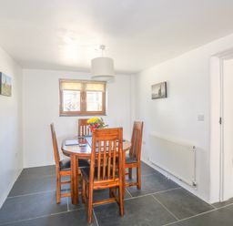A dining room with wooden table and chairs next to a window and wooden door at Lower West Curry Cottage Launceston
